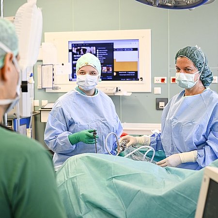 Drei Personen aus der Chirurgie operieren Patienten | Großer Monitor im Hintergrund | Foto@Karsten Klama